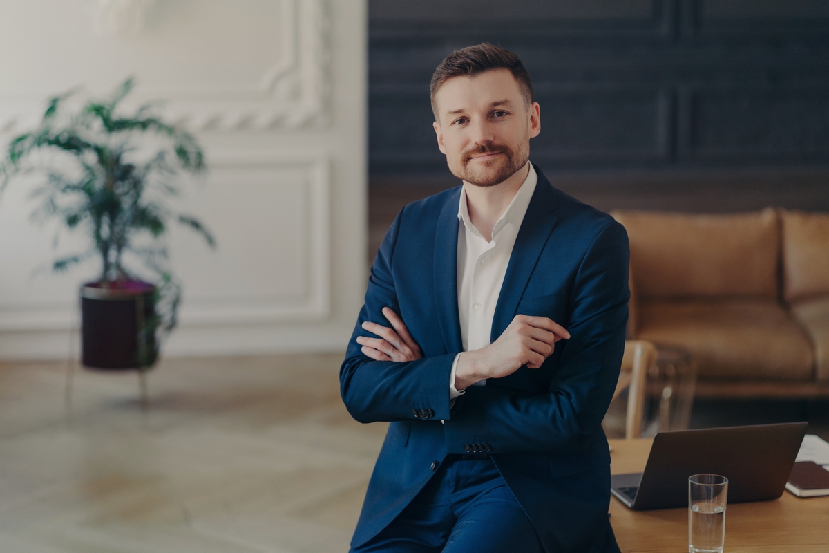 Portrait of successful confident businessman leaning on his office desk