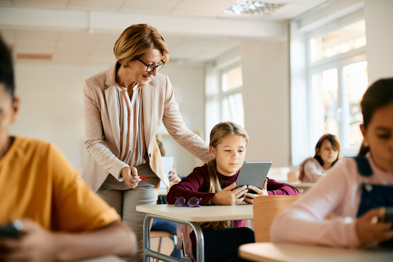 Senior teacher assisting schoolgirl in using digital tablet during a class at school.