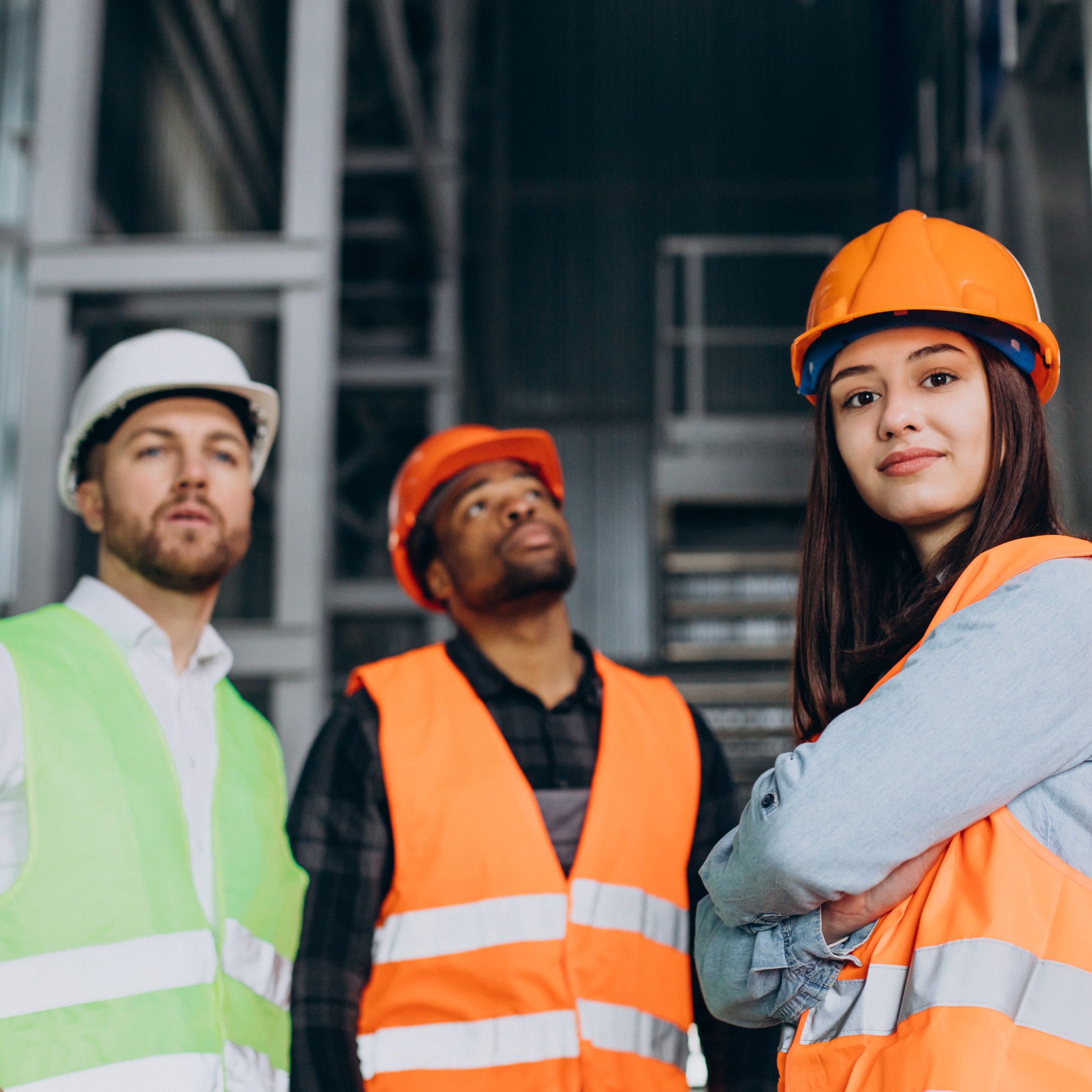 Three factory workers in safety hats discussing manufacture plan