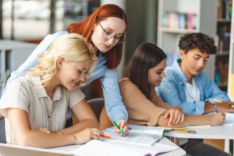 Attractive young school teacher wearing stylish eyeglasses holding pen showing something
