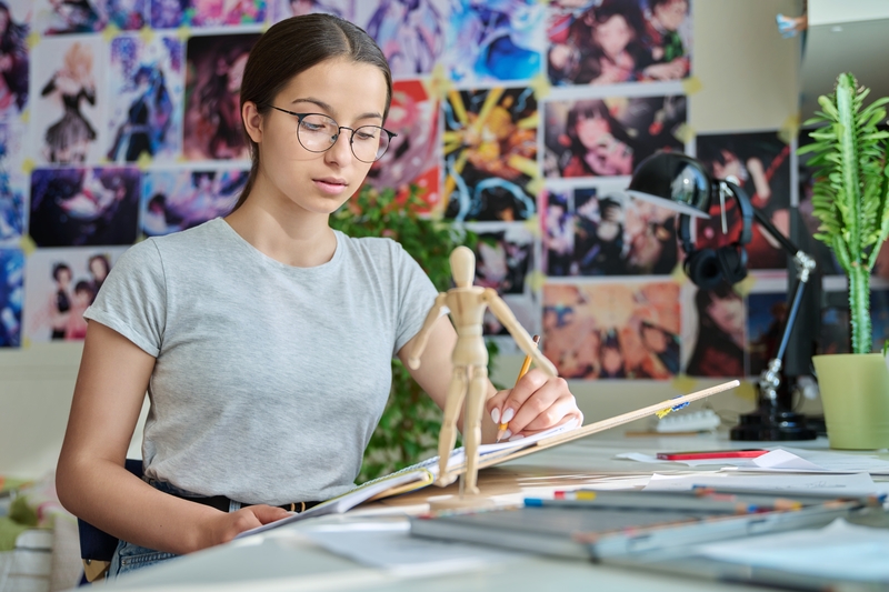 Teenage creative girl artist drawing with a pencil, sitting at the table at home