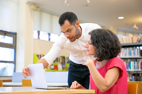 Instructor checking student work in library